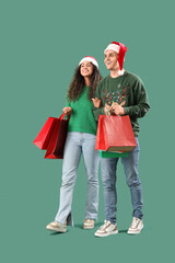 Happy young couple in Santa hats with shopping bags on green background