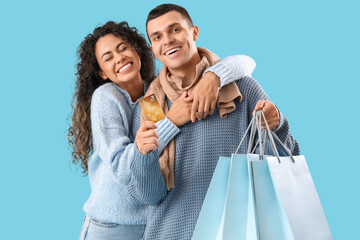 Happy young couple with credit card and shopping bags on blue background