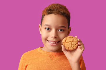 Cute little African-American boy with cookie on purple background