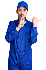 Middle age handsome man wearing mechanic uniform asking to be quiet with finger on lips pointing with hand to the side. silence and secret concept.