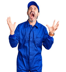 Middle age handsome man wearing mechanic uniform crazy and mad shouting and yelling with aggressive expression and arms raised. frustration concept.