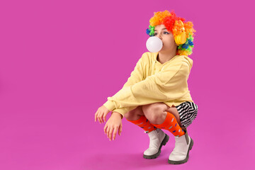 Trendy girl in clown costume blowing bubble gum on purple background