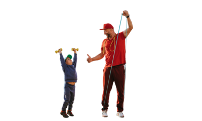 Mid aged bearded caucasian man in sportswear training with little son on beach against transparent background, shows thumb up gesture to boy. Preschooler boy lifts up dumbbells looks at father