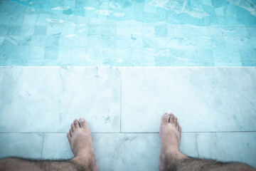 Relaxing man with his feet on poolside at swimming pool. Close up