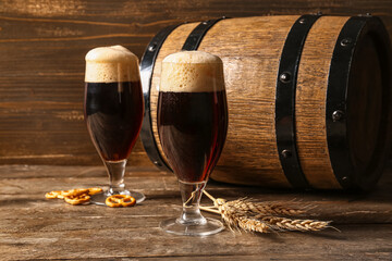 Glasses and barrel of cold dark beer with wheat and pretzels on table against wooden background