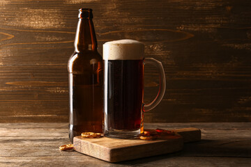 Mug and bottle of cold dark beer with pretzels on table against wooden background