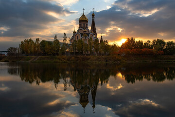 Fototapeta na wymiar Orthodox church on the shore of a pond in the Kazakh city of Almaty at sunset