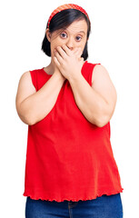 Brunette woman with down syndrome wearing casual clothes shocked covering mouth with hands for...