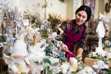Focused asian woman seller working in a store decorates a Christmas composition with candles