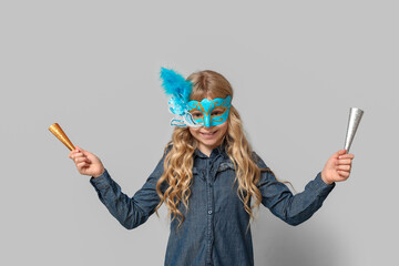 Cute little girl with noisemakers wearing carnival mask on light background