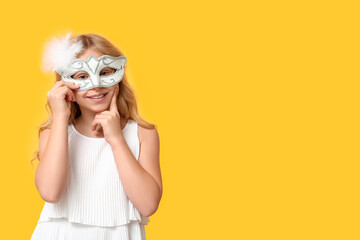 Thoughtful little girl wearing carnival mask on yellow background
