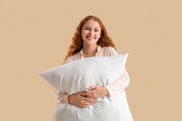 Beautiful young woman with white soft pillow on beige background