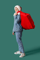 Happy young man in Santa hat with bag of gifts on green background