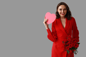 Happy young woman with bouquet of roses and red paper heart on grey background
