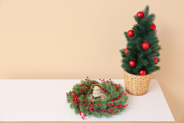 Dresser with Christmas tree in pot and wreath near beige wall