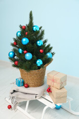 Sledge with Christmas tree in pot and gifts near blue wall