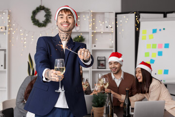 Young man with champagne and sparkler celebrating New Year at corporate party in office