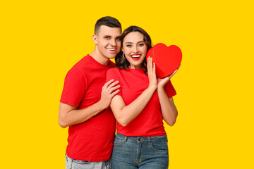 Loving young couple with gift box on yellow background. Celebration of Saint Valentine's Day