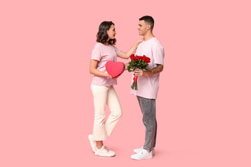 Loving young couple with gift box and bouquet of beautiful roses on pink background. Celebration of...