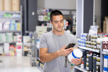 Focused interested young man choosing painting materials in construction hypermarket, using...