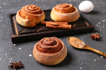 Wooden board with tasty cinnamon rolls on black background
