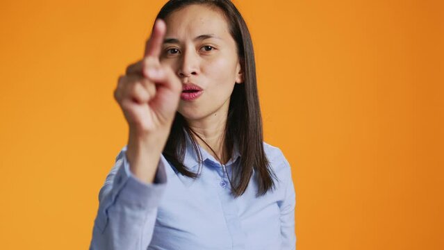 During the shot, pleased filipino girl points index finger at the lens. Confident young woman with calm mood using charm and personality, standing over orange background illustrating stuff.