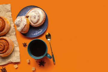 Plate with tasty cinnamon rolls and cup of tea on orange background