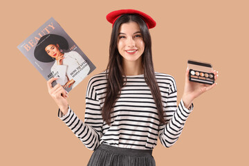 Young woman with beauty magazine and eyeshadows on beige background