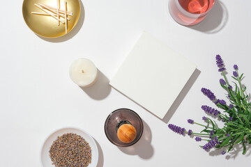 Top view of a lavender bouquet, a white podium, a bottle of essential oil diffuser, a candle, matches and dried lavender arranged on a white background. Copy space.
