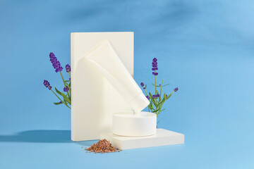 Front view of a cosmetic tube is placed on a white platform, next to it is fresh and dried lavender on a blue background. Lavender has a purple color and unique scent.