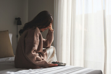Rear view of a sad woman after reading bad news on smartphone in bedroom - obrazy, fototapety, plakaty