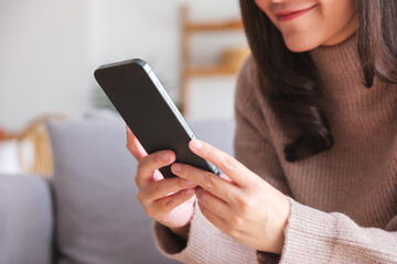 Closeup image of a young woman holding and using smart phone at home