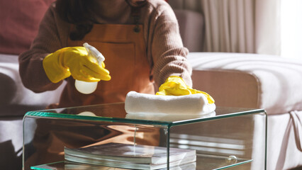 Closeup image of a woman wearing protective glove, wiping and cleaning glass table at home