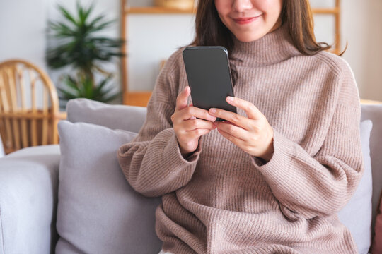 Closeup image of a young woman holding and using smart phone at home