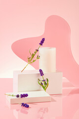 A candle is placed on a white podium with lavender flowers, next to an acrylic sheet on a pastel pink background. Display products with ideal space.