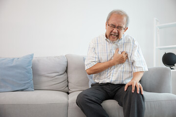senior elderly man have a chest pain or suffering from heart attack on a sofa