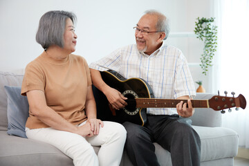 senior couple playing acoustic guitar together on sofa
