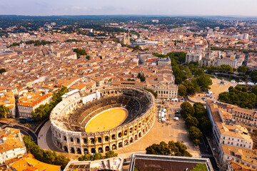 Fototapeta premium Drone view of ancient Roman amphitheatre Arena of Nimes on background of reddish tiled roofs of residential buildings on summer day, France