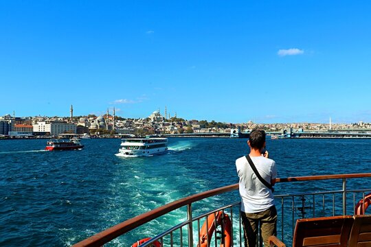 a young man on board a ferry sailing along the Bosphorus takes pictures of the sights of Istanbul on his phone camera