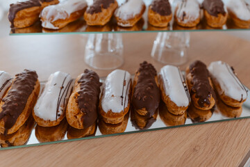 Eclairs with white and chocolate icing are laid out in a row on a mirror surface, display in a store.