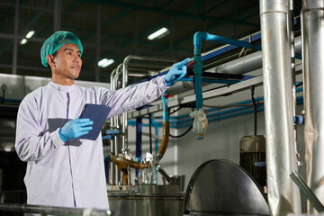 worker pointing to something beside large industrial pot in the beverage factory