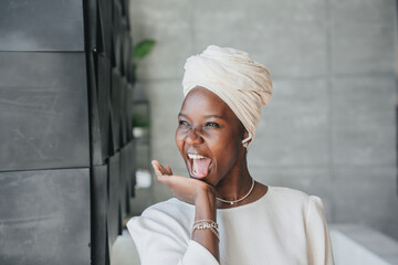 Excited African girl in white turban and traditional dress shouting looks at window with wide...