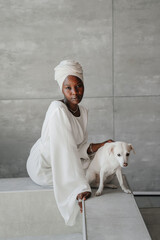 Vertical shot of young African woman in white turban and traditional dress sitting on bath with...
