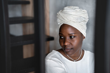 Sad African girl in white turban sitting at home looks aside, frustration, solitude. Unhappy young...