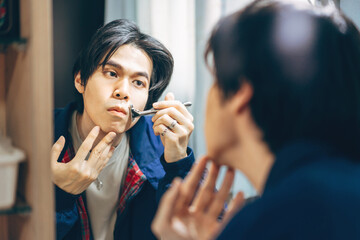 Young adult asian man using razor shaving in this mirror reflection