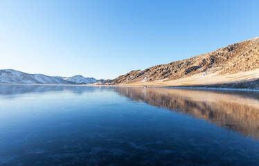 Winter landscape of frozen Baikal Lake in January at sunset. Tourists come to shore of iced bay to...