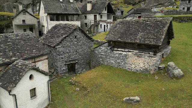 Aerial drone forward moving shot flying over old empty village houses along the slope in Cavergno, District of Vallemaggia, Canton of Ticino in Switzerland.