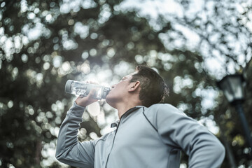 Young sport man drink water after jogging, running in the park. Sport thirsty and resting after exercise. Health and Lifestyle in big city life concept.