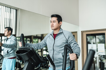 A man using elliptical trainer in fitness gym.  Fitness, workout, sport and health concept. - obrazy, fototapety, plakaty