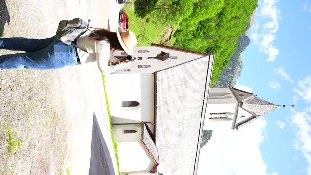 Rear shot of a tourist woman filming a church in Sottoguda, Italy. Vertical